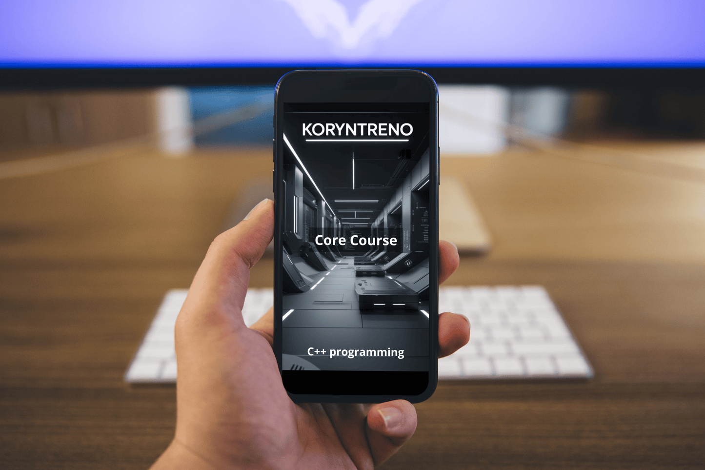 Hand holding a smartphone with Koryntreno C++ course on screen, blurred office desk in background