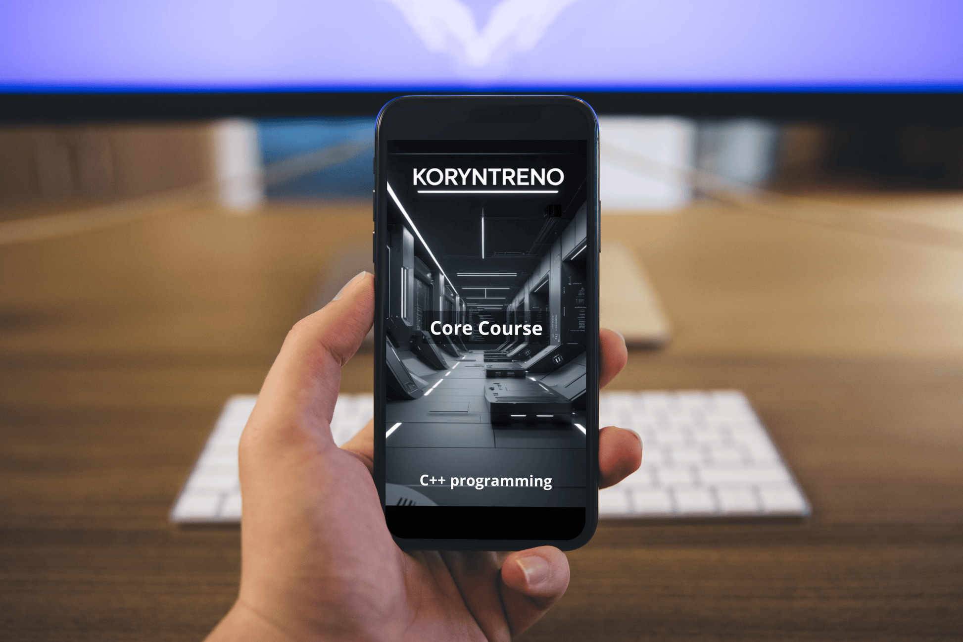 Hand holding a smartphone with Koryntreno C++ course on screen, blurred office desk in background