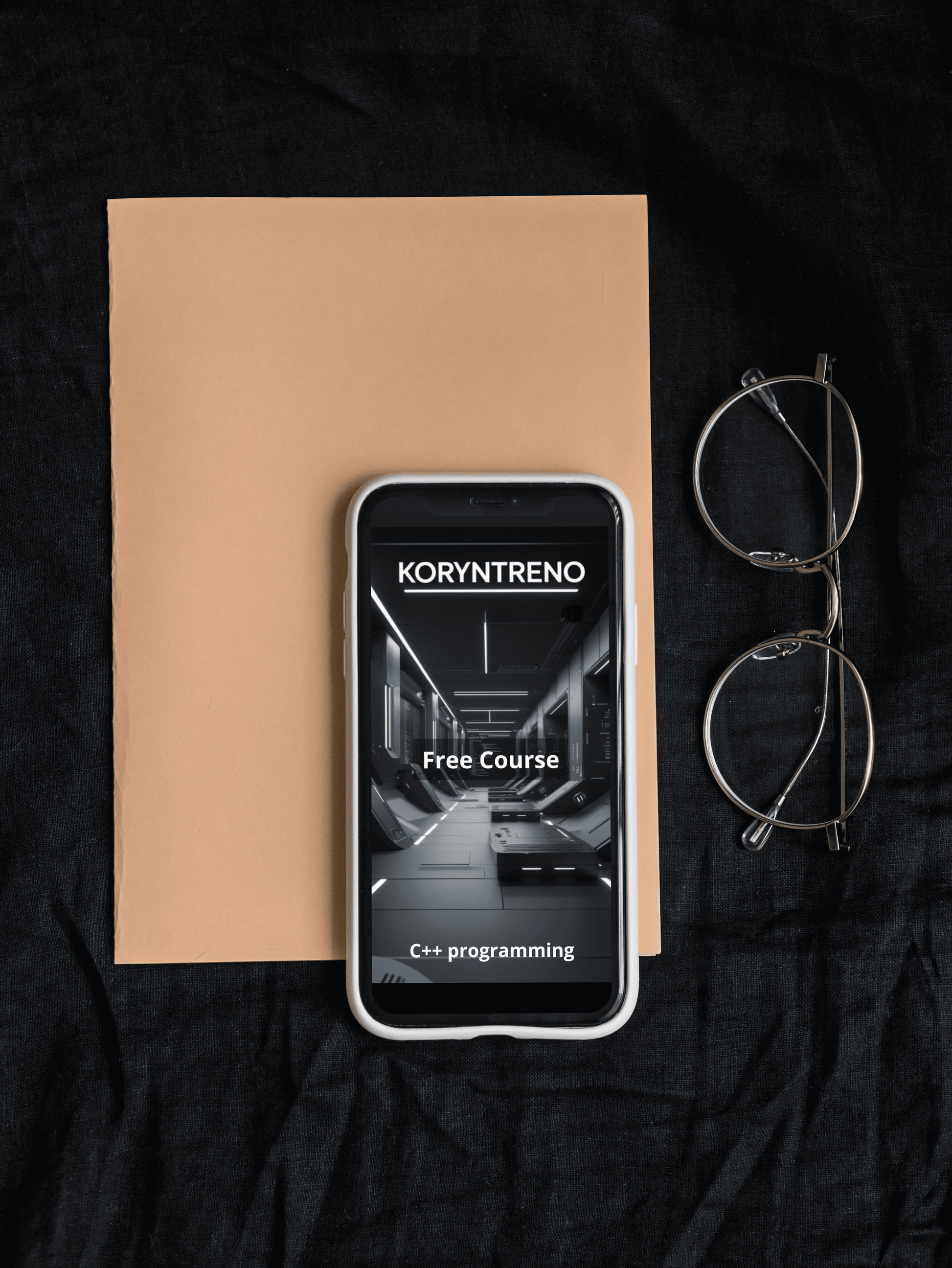 Phone displaying a Koryntreno C++ course with a book and eyeglasses on a dark surface