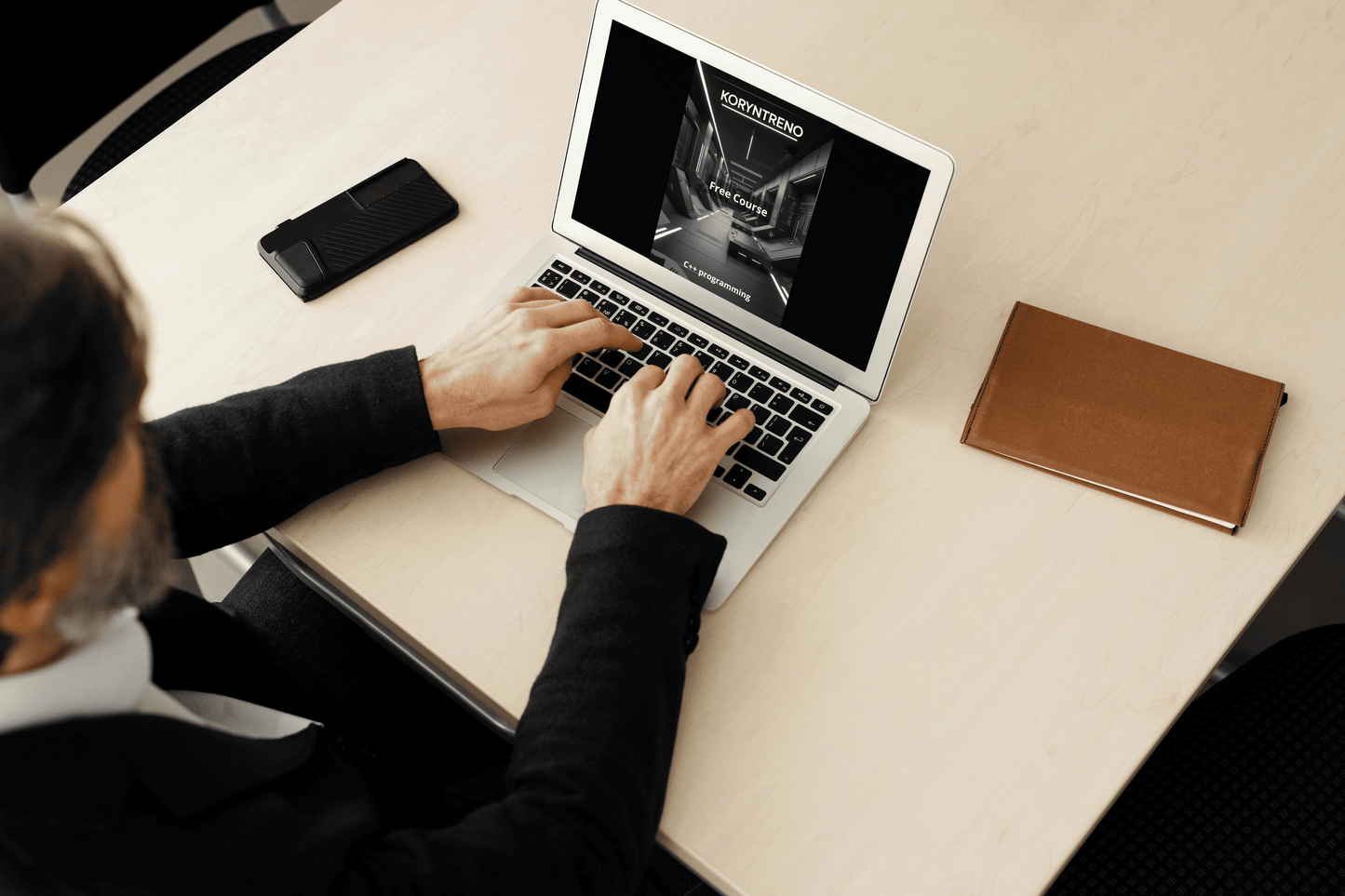 Person using a laptop on a desk with a phone and notebook nearby