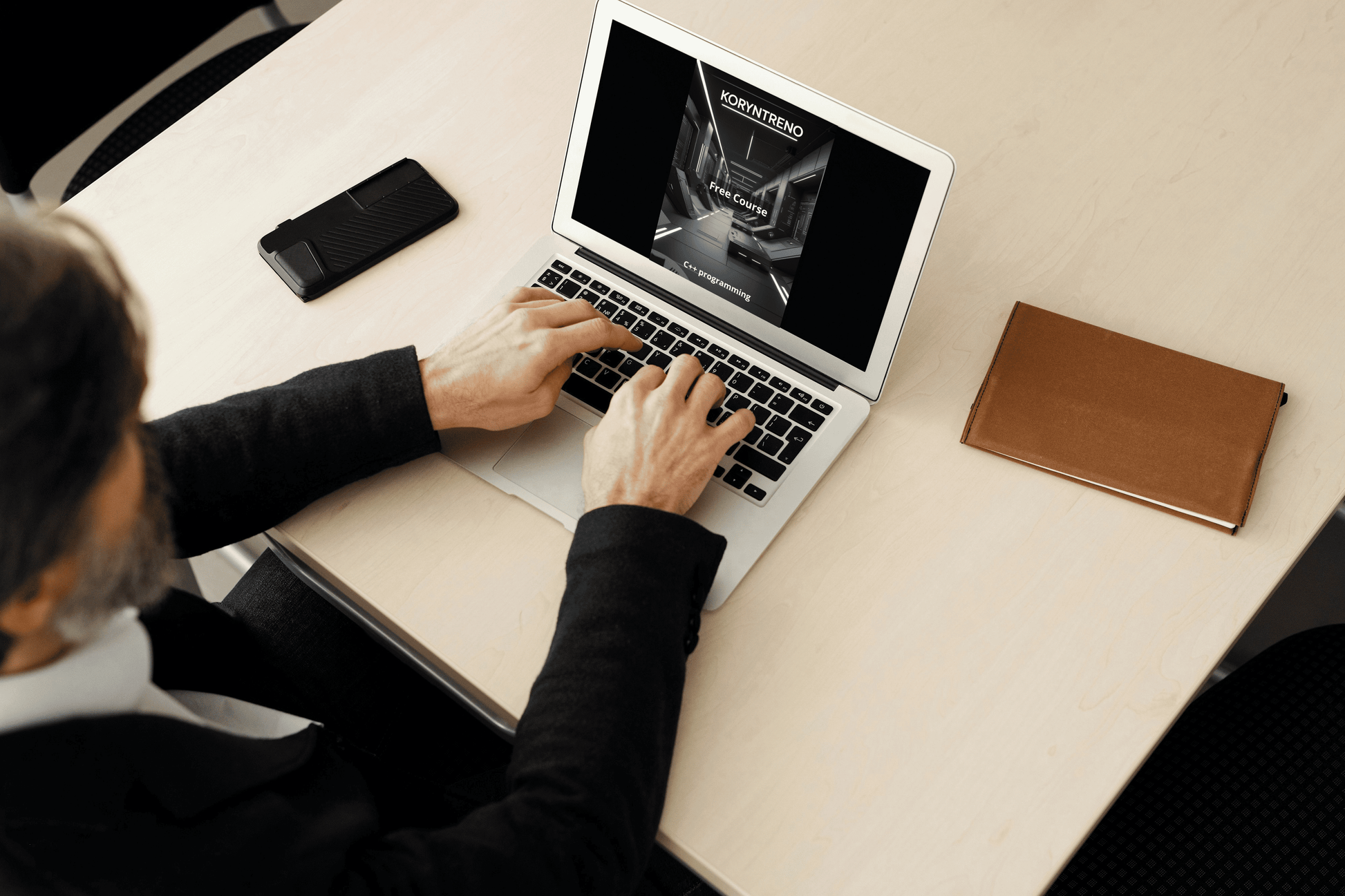 Person using a laptop on a desk with a phone and notebook nearby