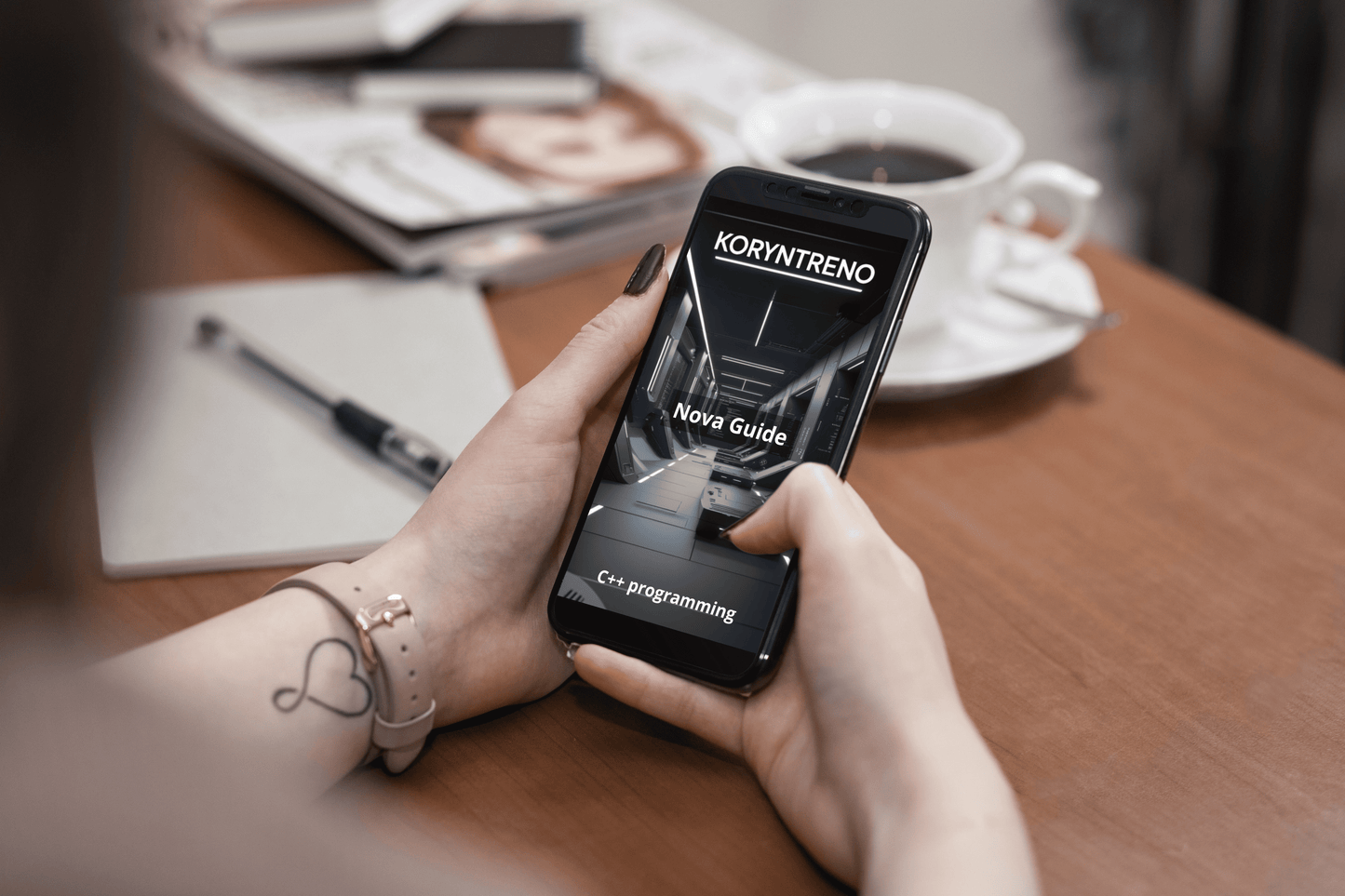 Person holding a smartphone with Koryntreno C++ course  on a table with coffee and magazine
