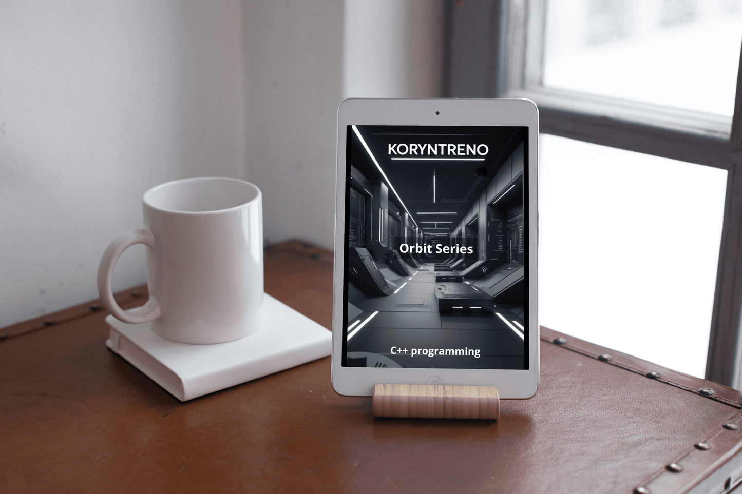 Tablet on a stand displaying 'Koryntreno' app with a white mug and notebook on a wooden surface.