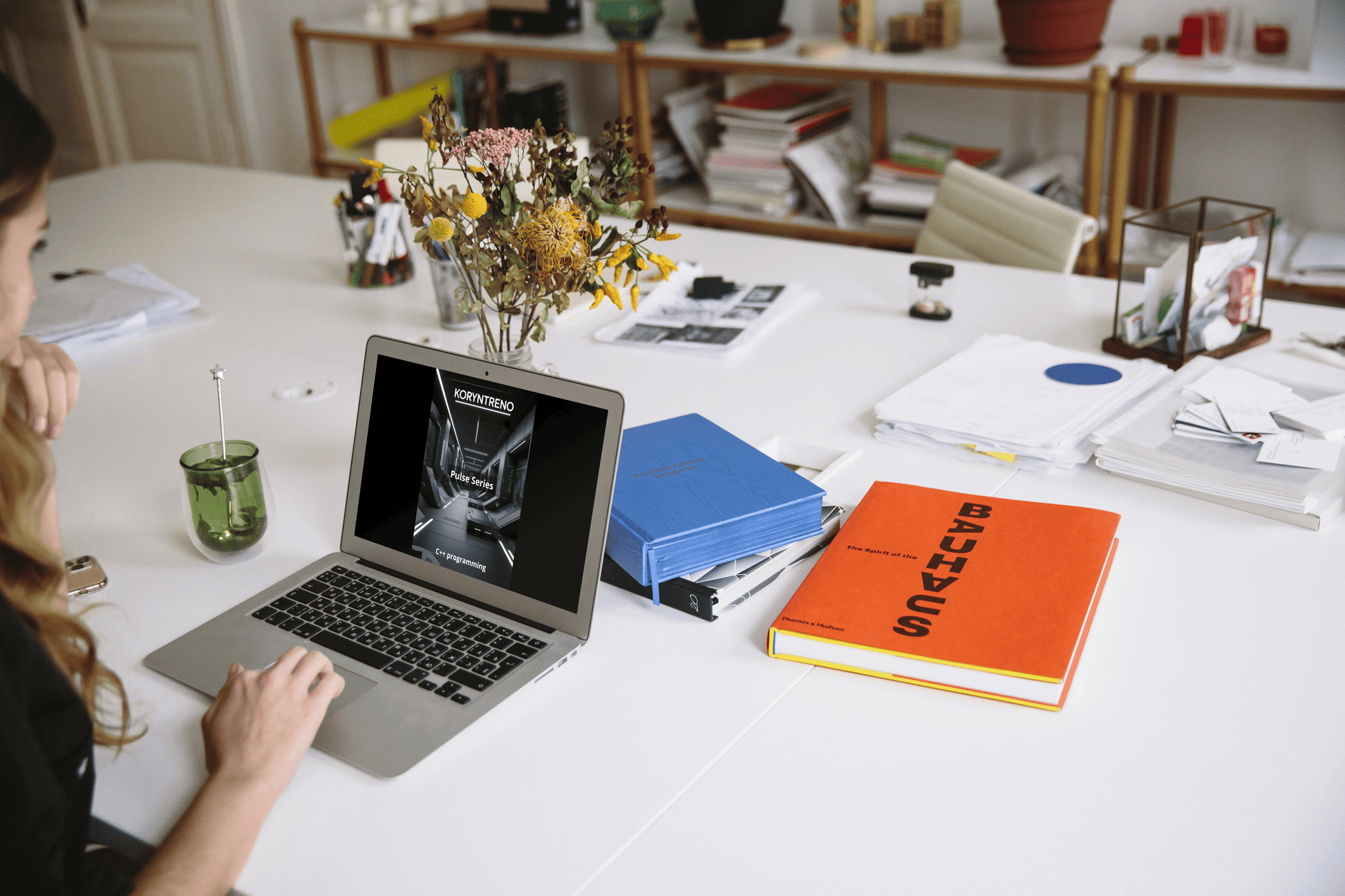 Person using a laptop with C++ course on a desk with books, a notebook, and decorative items.