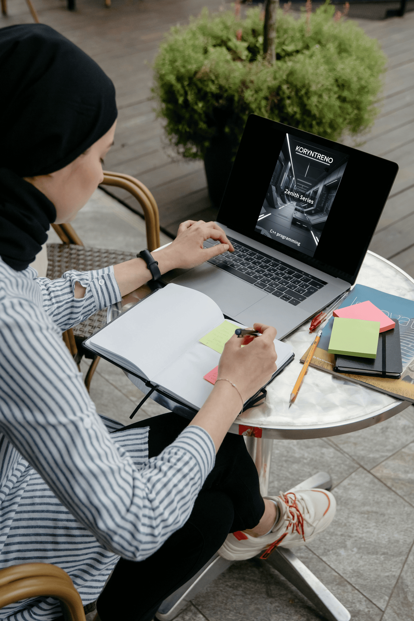 Person working on a laptop outdoors with a plant and table in the background